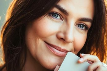 Девушка сидит у окна с чашкой чая, улыбается и думает о себе